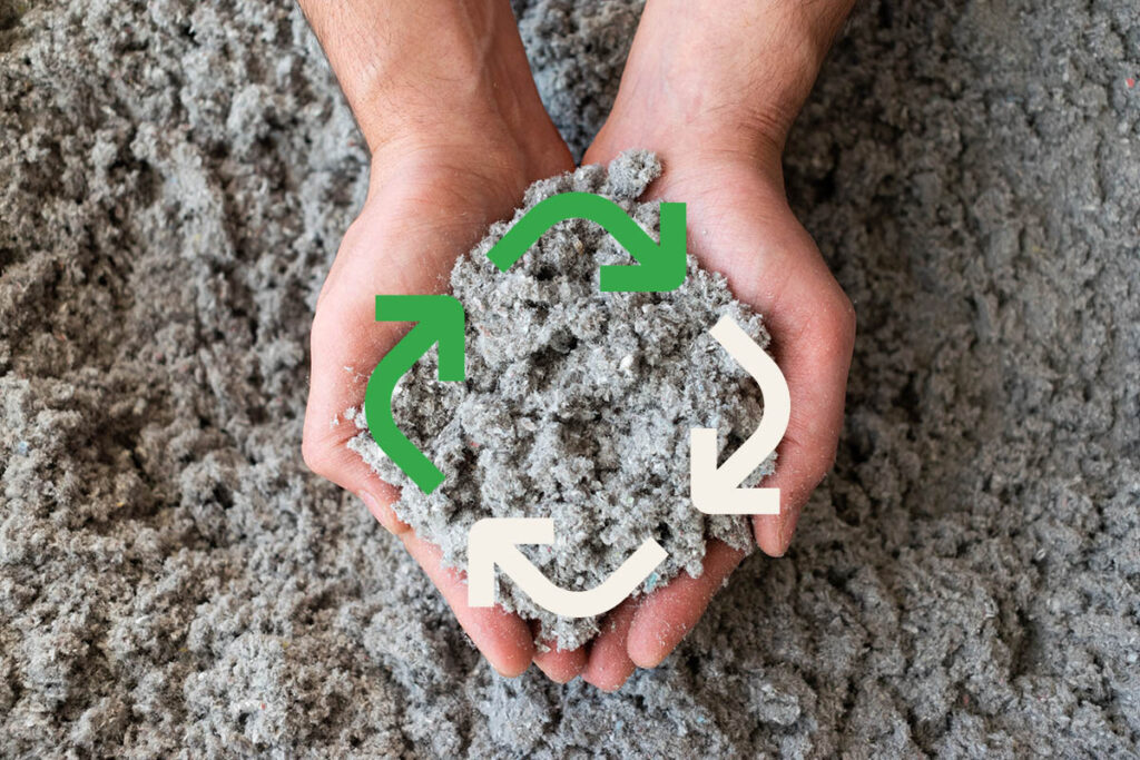 Nahaufnahme einer umweltfreundlichen Zelluloseisolierung, die in der Hand gehalten wird. Darüber ein Recycling-Symbol.